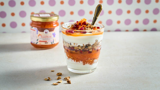 Glas kwarkparfait met Perzische wortelspread, granola en fruit, met een pot Wortel Wonder op de achtergrond.