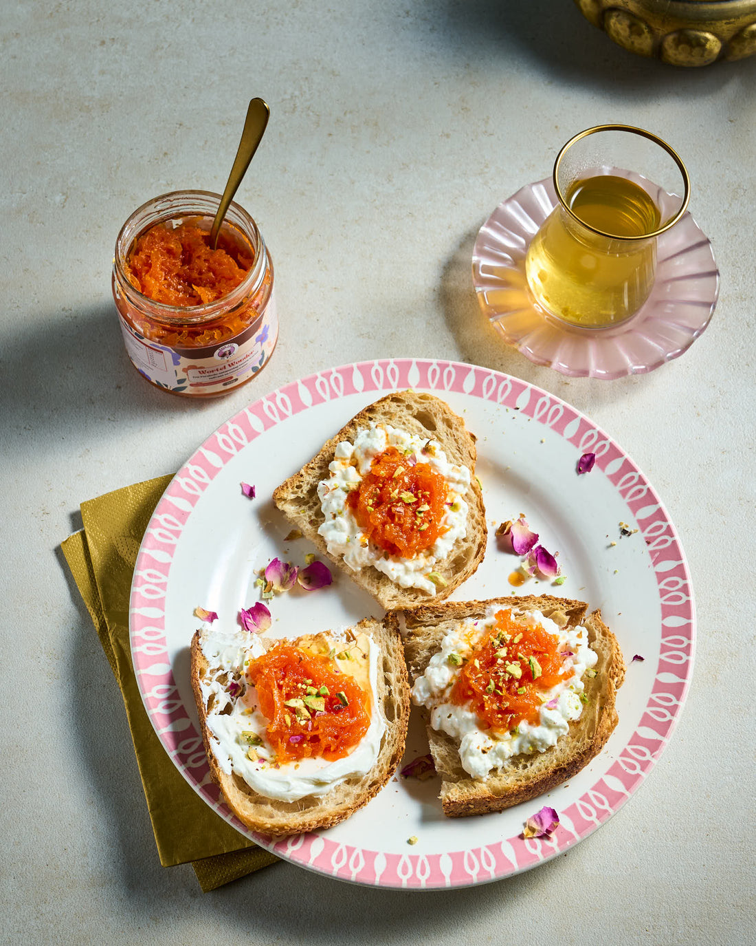 Bord met toast, cottage cheese en Perzische wortelspread, geserveerd naast een glas Perzische thee.