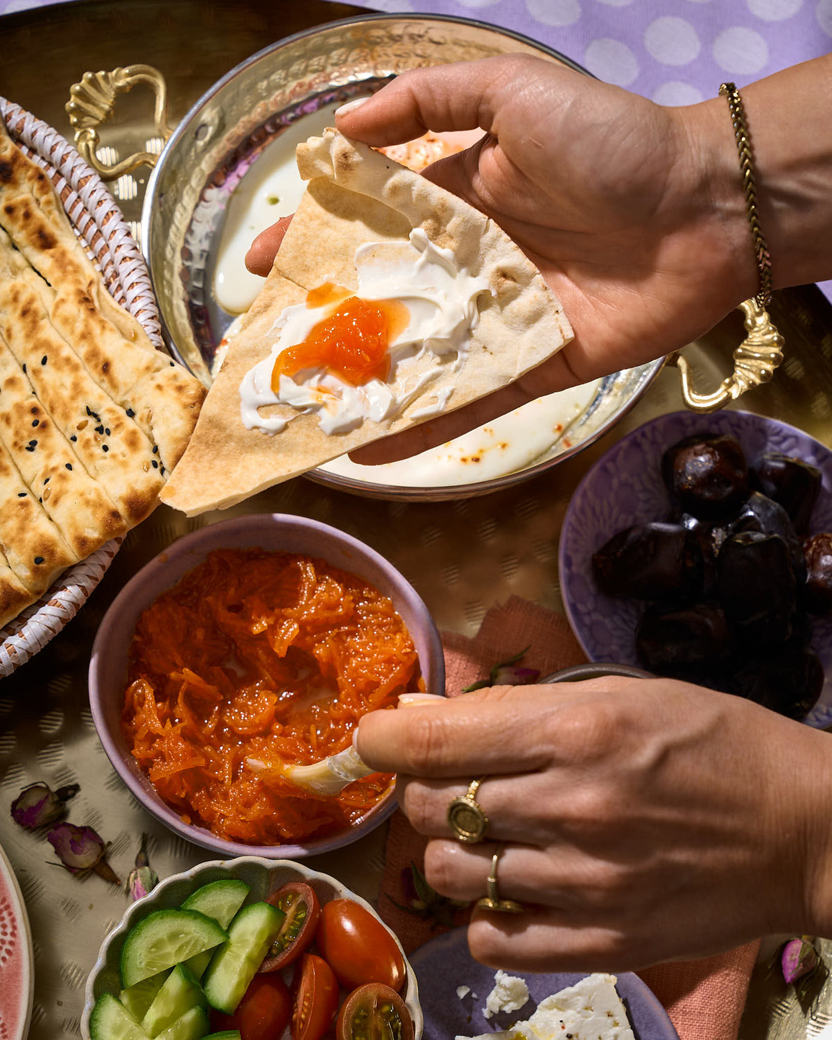 Een hand houdt lavash brood vast met daarop Iraanse worteljam en schept met de andere hand de jam uit een kom.
