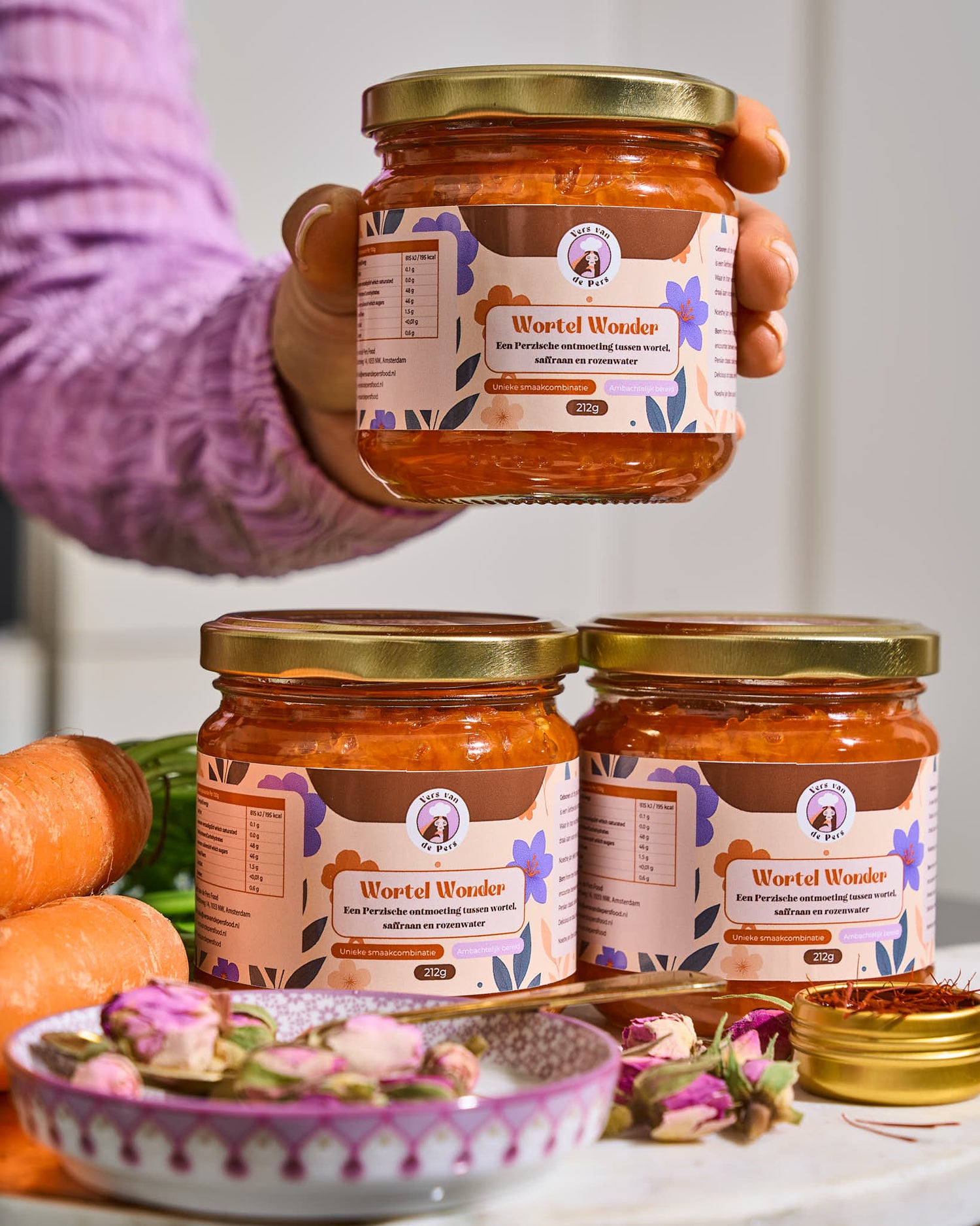 twee potten Wortel Wonder (Perzische worteljam) naast elkaar en een hand houdt een derde pot erboven vast