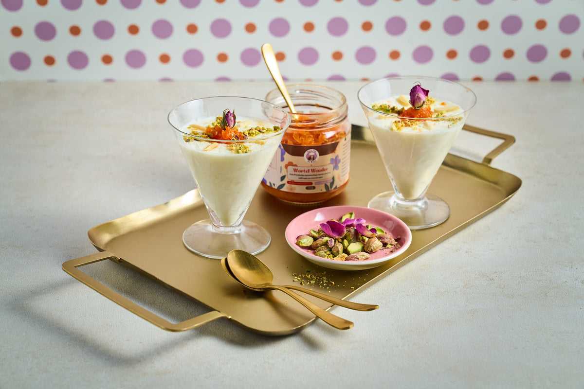 Twee glaasjes Ferni (Iraanse pudding) en pot Wortel Wonder (Perzische worteljam) met een lepel erin op een gouden dienblad